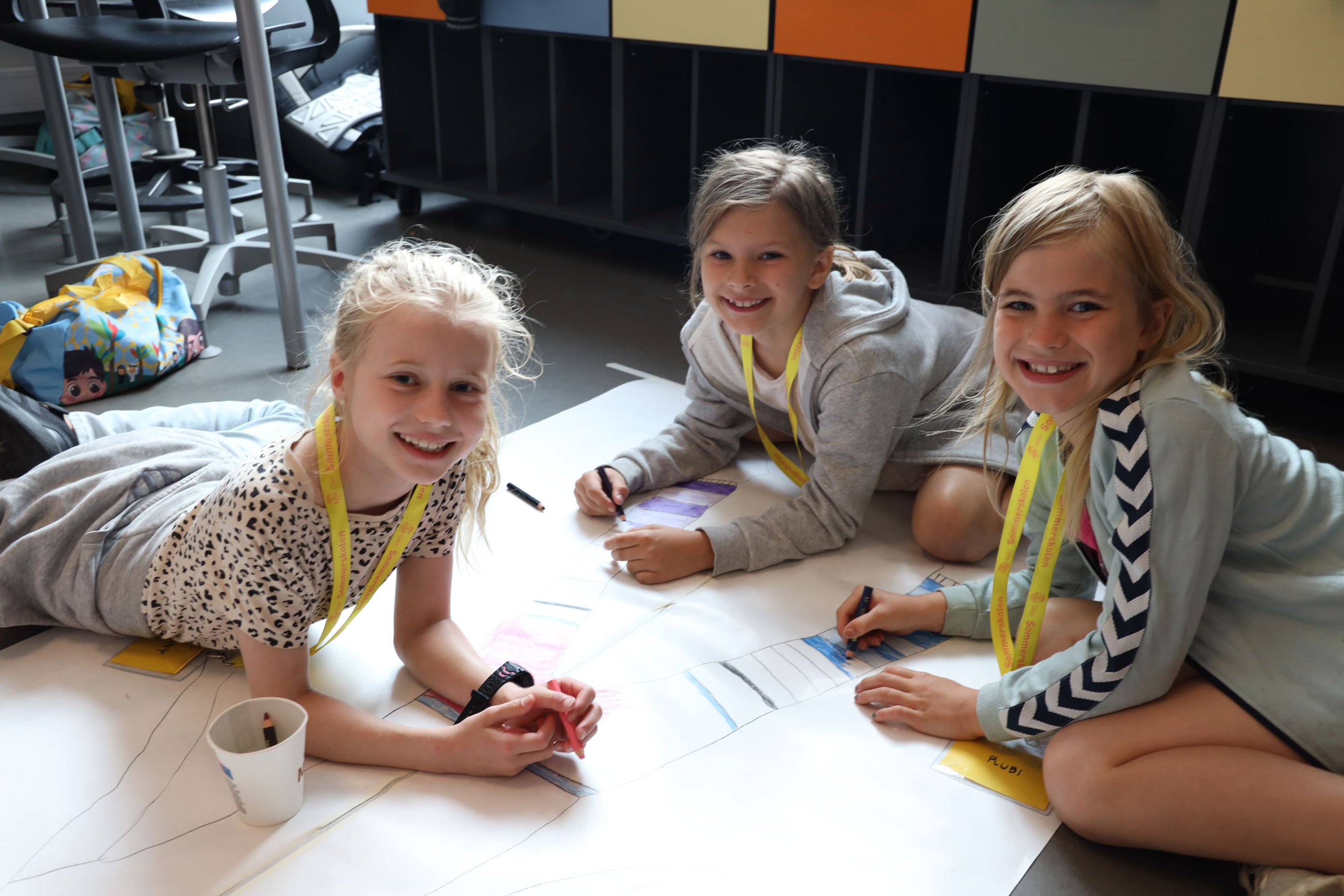 en gruppe barn som tegner på et ark på gulvet.