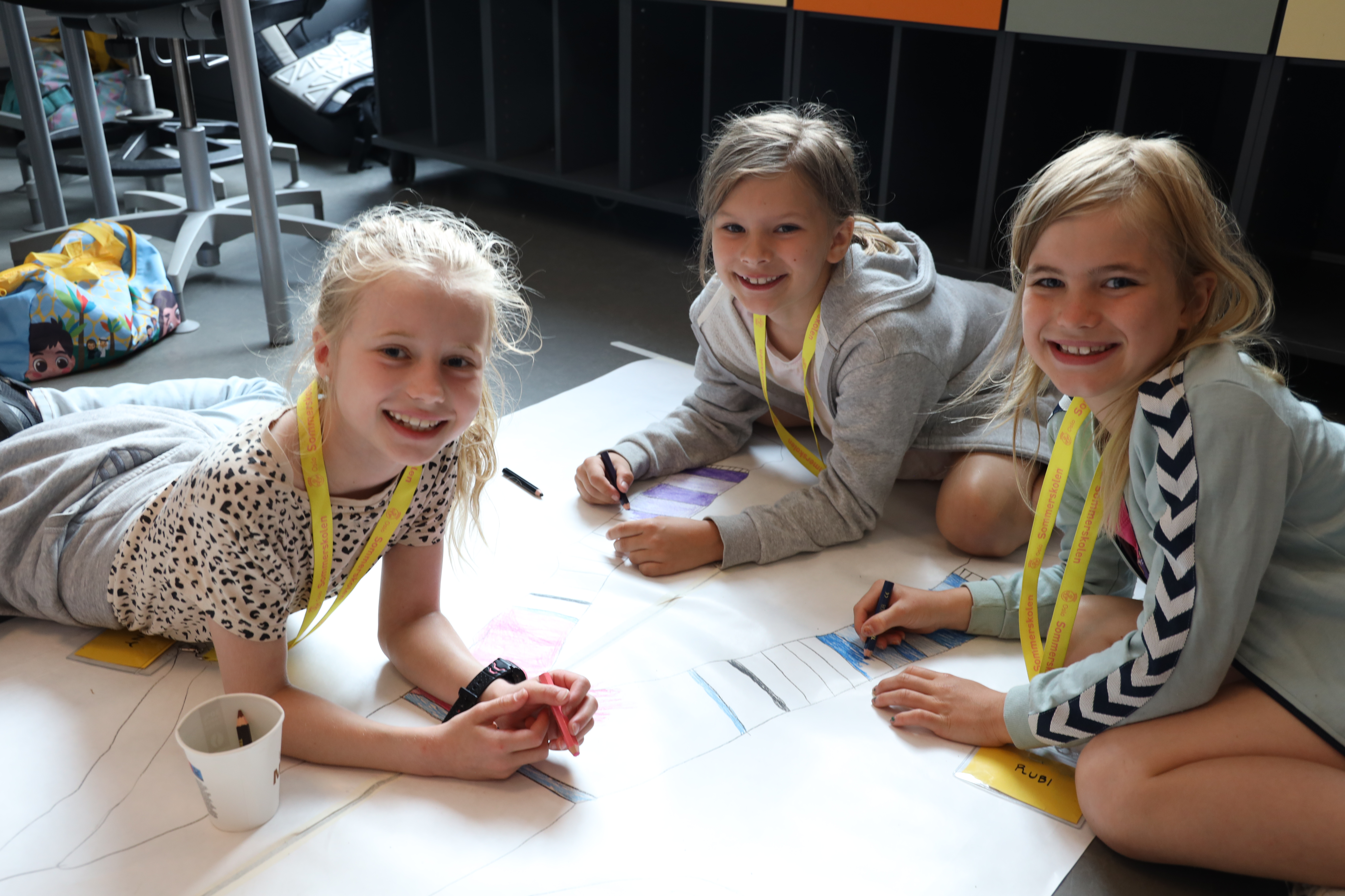 en gruppe barn som tegner på et ark på gulvet.